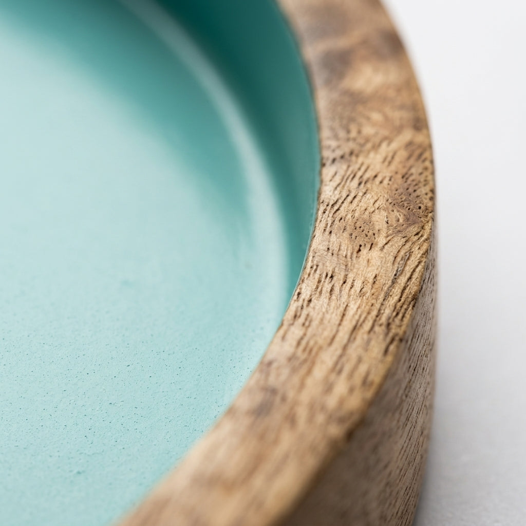 Close-up of a shallow round tray or dish with a smooth matte aqua interior and a natural wood rim on a white background.
